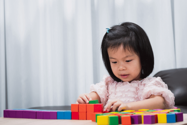 An Asian toddler is playing with the building blocks on the table.
