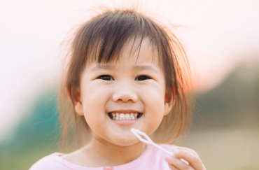 An Asian little girl smiles happily while blowing bubbles.