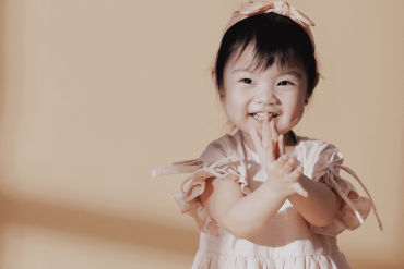 An Asian little girl is smiling happily in front of the camera.