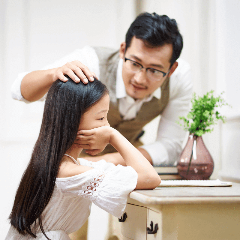 An Asian father is comforting his sad daughter.