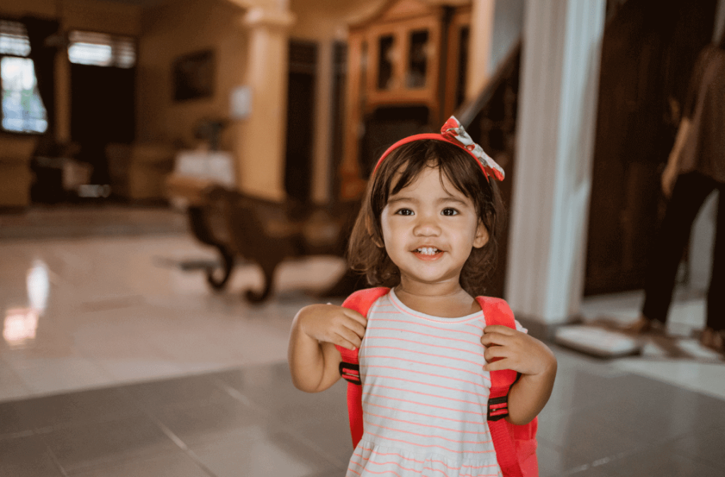 An Asian toddler is walking around with her backpack.