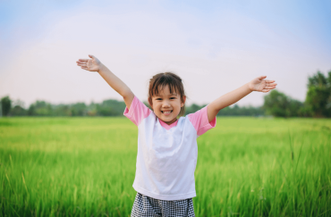 An Asian toddler is posing happily in front of the paddy field.