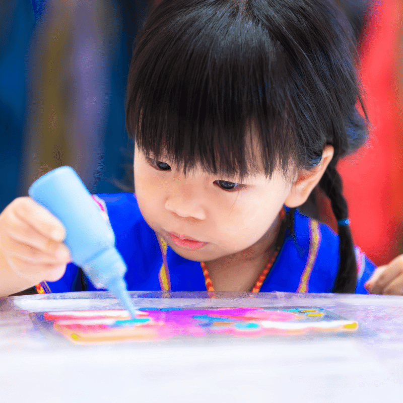 An asian toddler is making craft with the glitter glue.