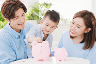 An Asian family is putting coins into a piggy bank.