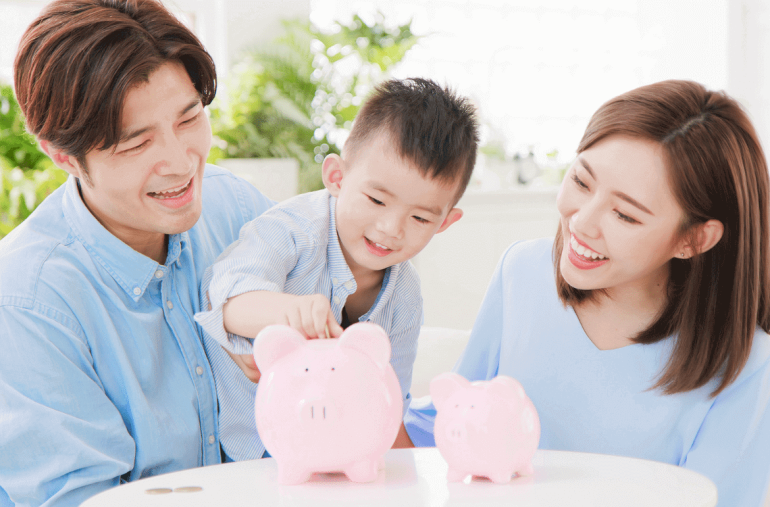 An Asian family is putting coins into a piggy bank.