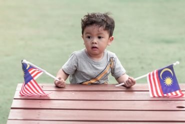A boy holding flags for Malaysia Day