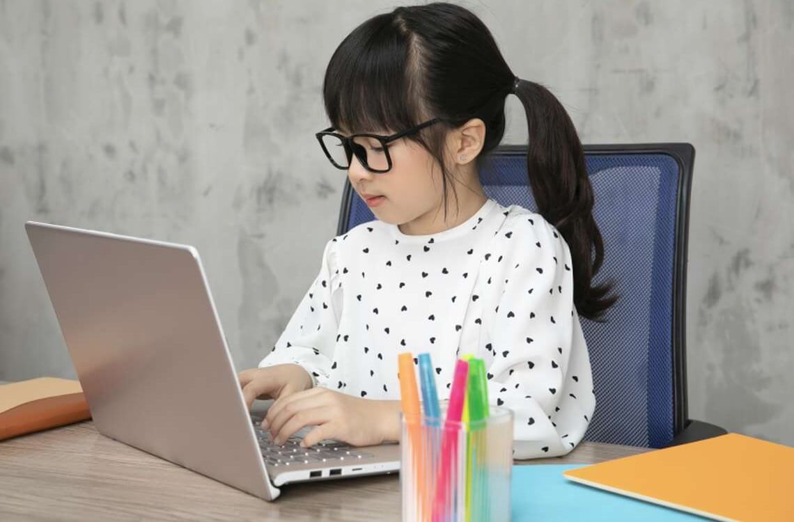 little girl with glasses studying with computer