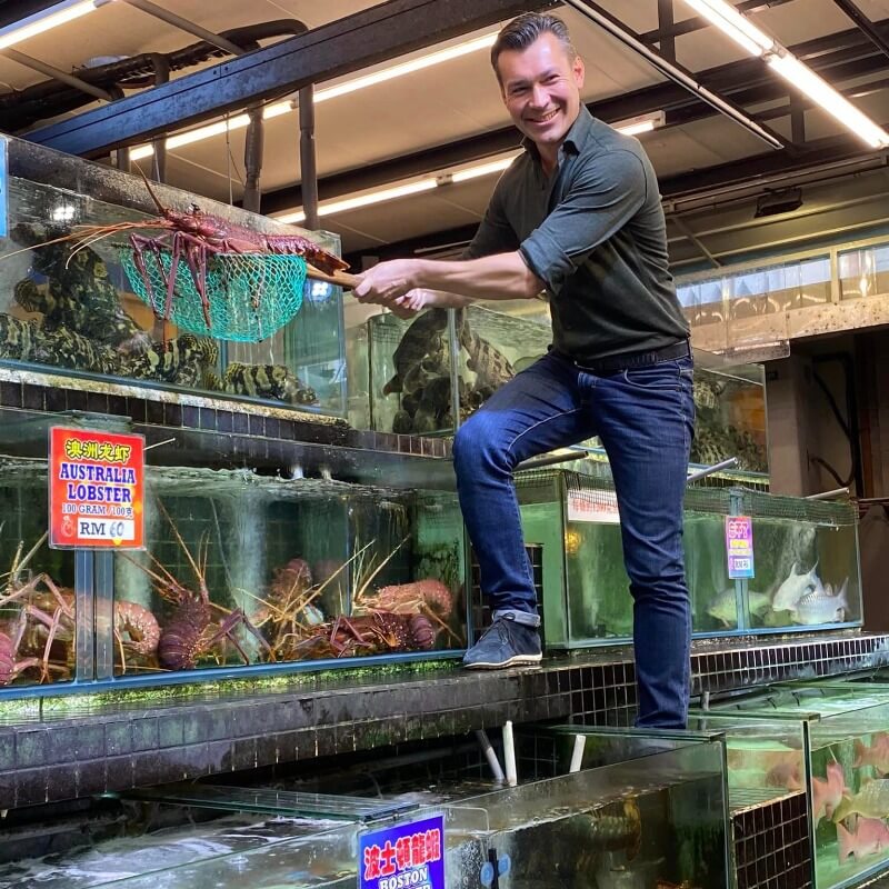 man standing over aquarium with lobster in net
