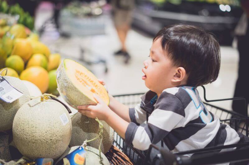 boy choosing melon grocery shopping