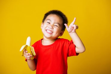 Little Boy In Red Shirt Eating Bananas