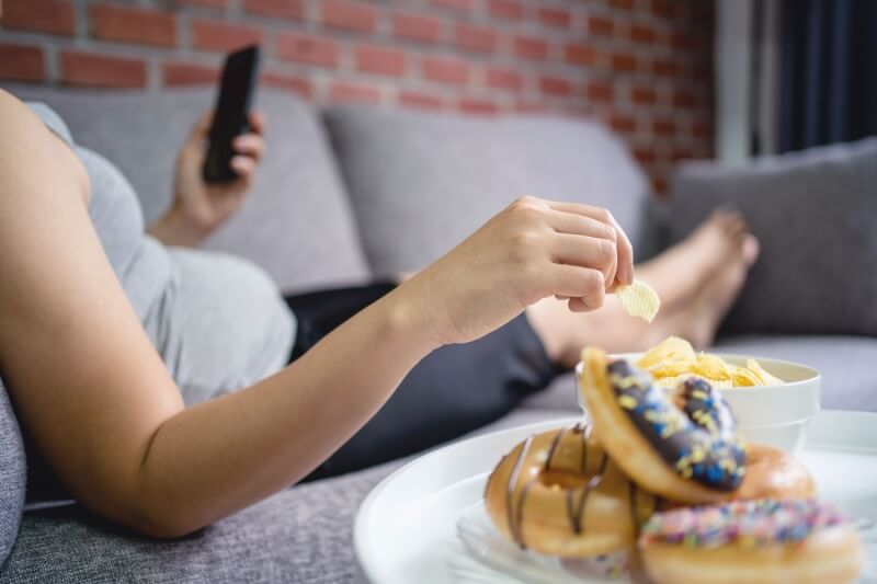 immune boosters woman being a couch potato eating unhealthy snacks