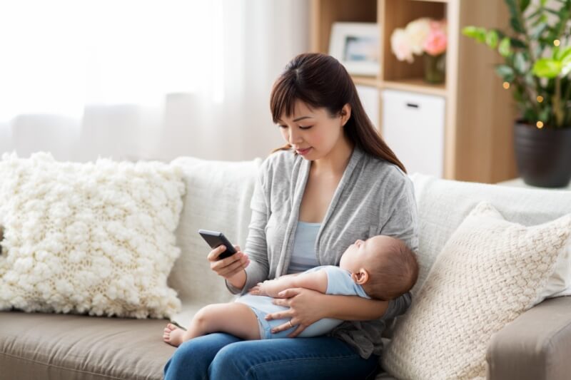 mother holding baby while looking at the phone