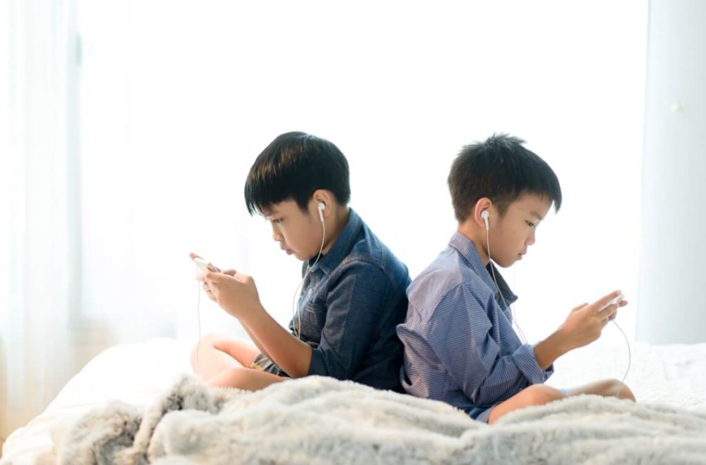 two boys using handphone and earphones