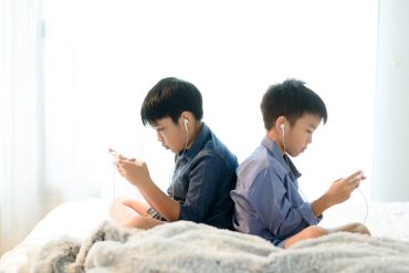 two boys using handphone and earphones