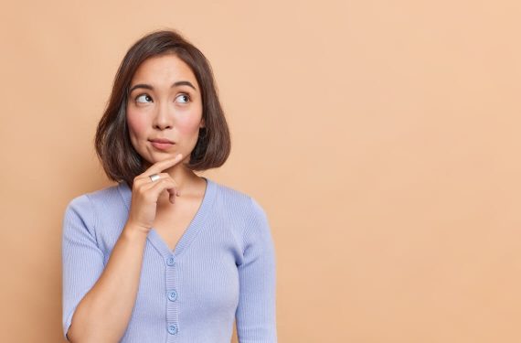 Asian woman keeps hand on chin wearing blue jumper