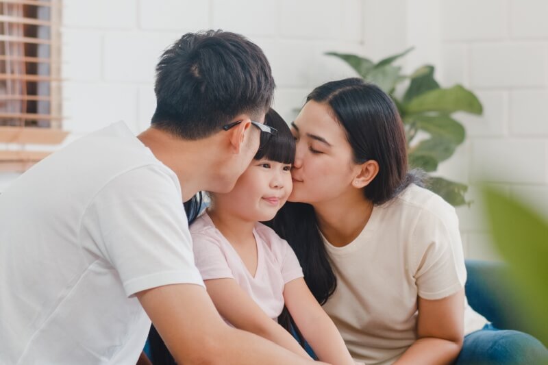 Asian family dad, mom and daughter embracing kissing on cheek