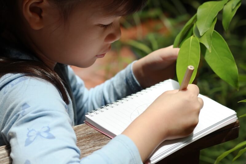 young girl in nature looking at leaf and taking notes