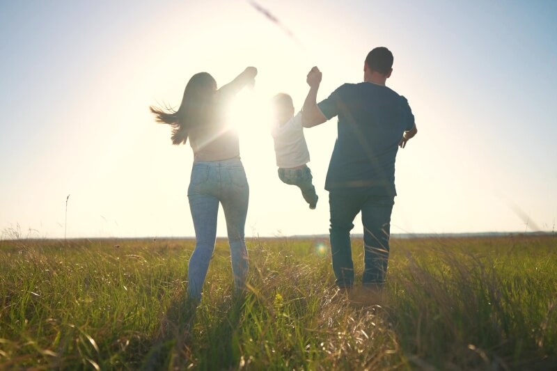 parents carrying child with sunset in the background