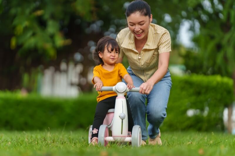 mother teaches her toddler how to ride bicycle