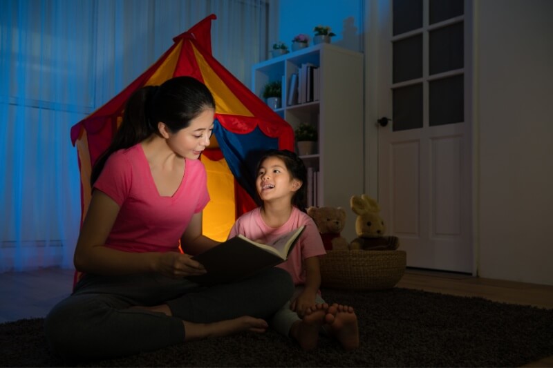 mummy sharing bedtime story with daughter with tent in background before bedtime