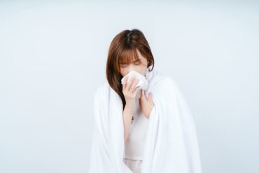 Asian woman sick and sneezing with tissue paper in bedroom