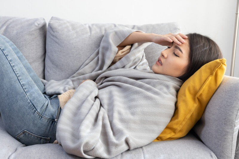 woman feeling unwell resting with blanket on the sofa