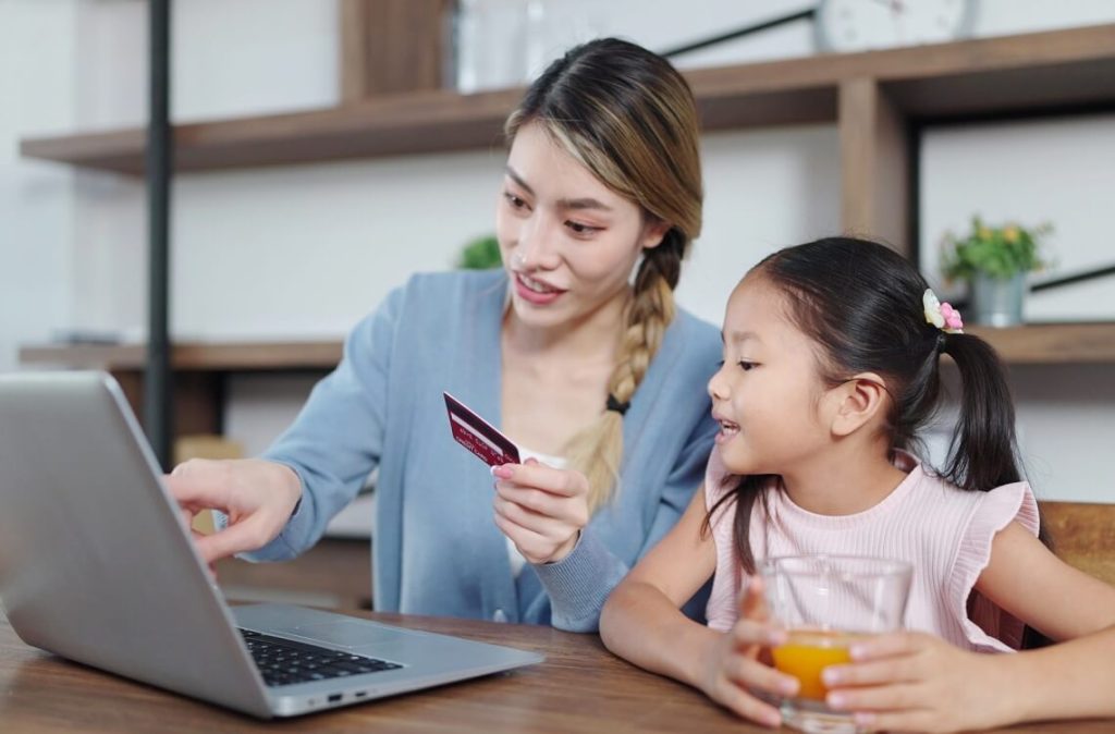 Mother showing daughter how to use debit card on the laptop