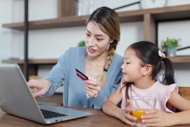 Mother showing daughter how to use debit card on the laptop