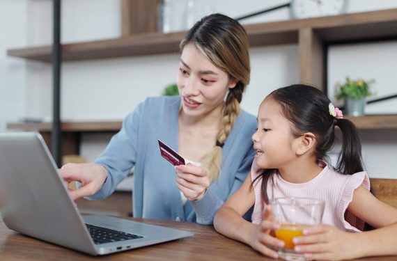 Mother showing daughter how to use debit card on the laptop