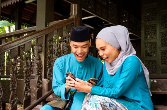 couple in blue traditional malay clothing looking at the handphone