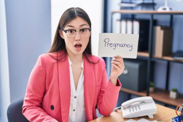 woman in pink jacket showing pregnancy sign