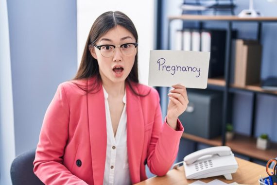 woman in pink jacket showing pregnancy sign