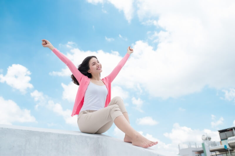 young woman relaxing under blue sky on rooftop with her hands raised towards sky