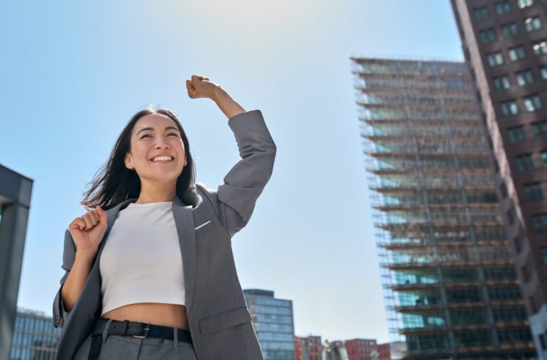 business woman winner wearing suit standing on street, raising hands, feeling power, motivation, energy, celebrating career financial success career comeback for mothers