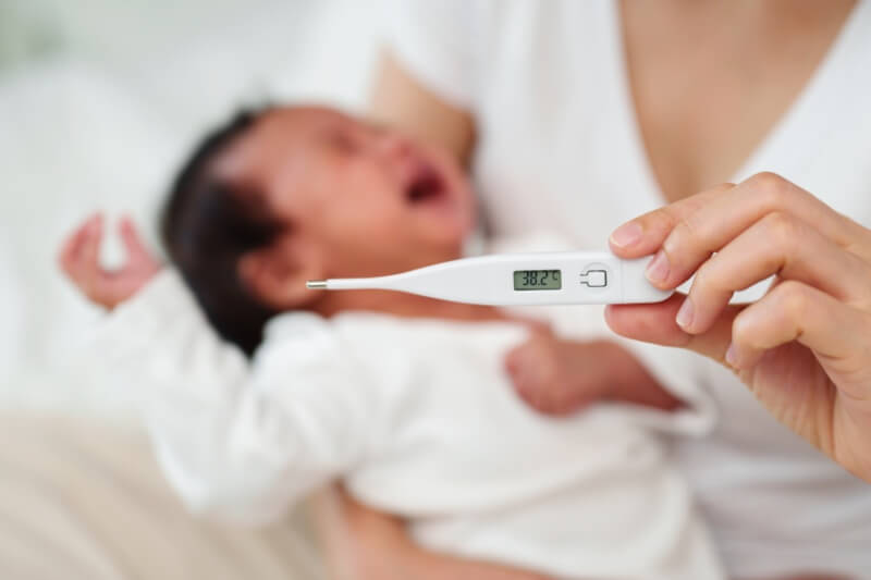 mother holding thermometer newborn baby crying