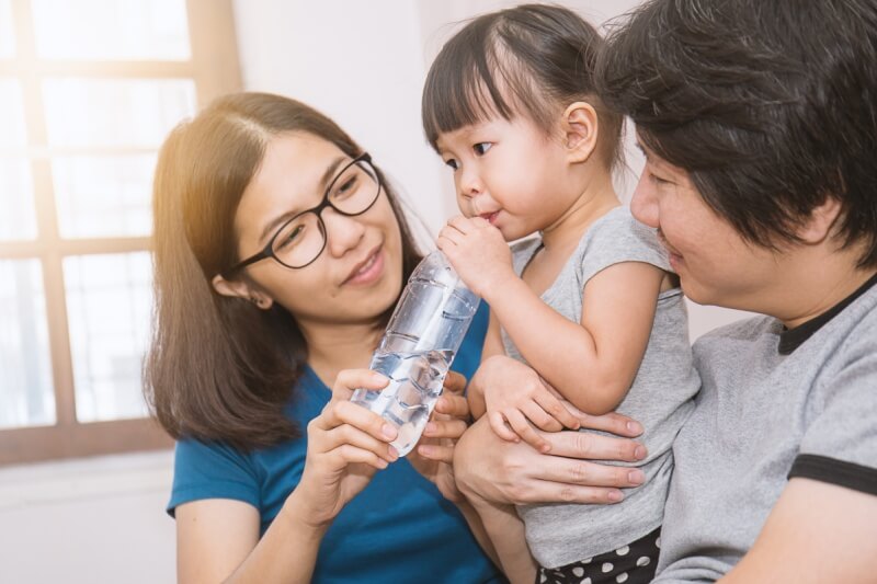 Parents giving little daughter a bottle with drink