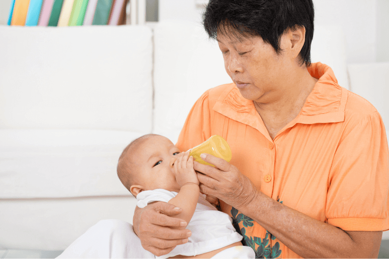 helper babysitting child feeding baby in milk bottle