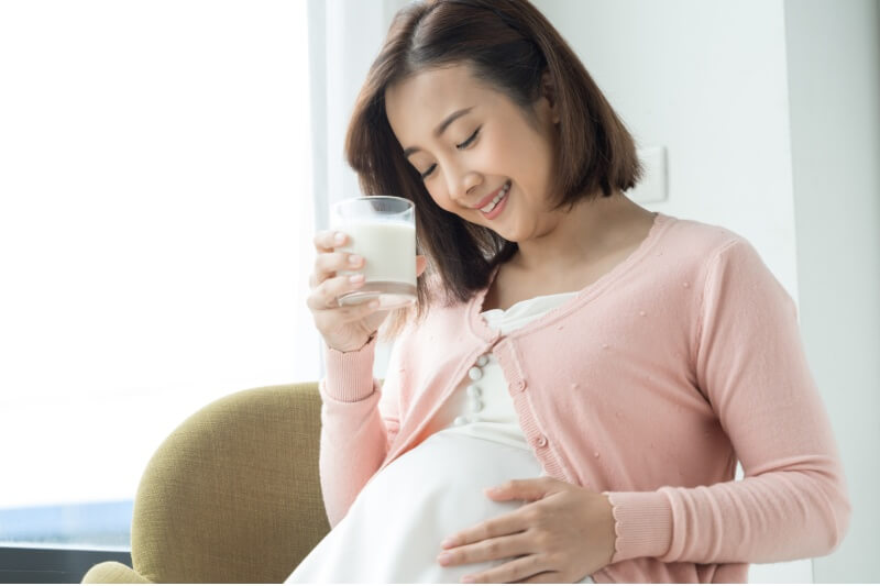 pregnant woman drinking glass of milk wearing maternity clothes 