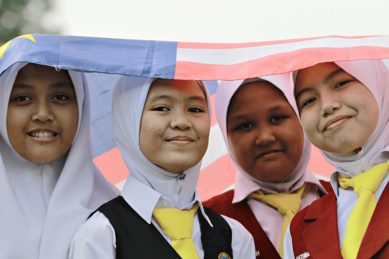 Four primary school girls standing under the Malaysian National Flag also known as "Jalur Gemilang" during Malaysia Day celebration