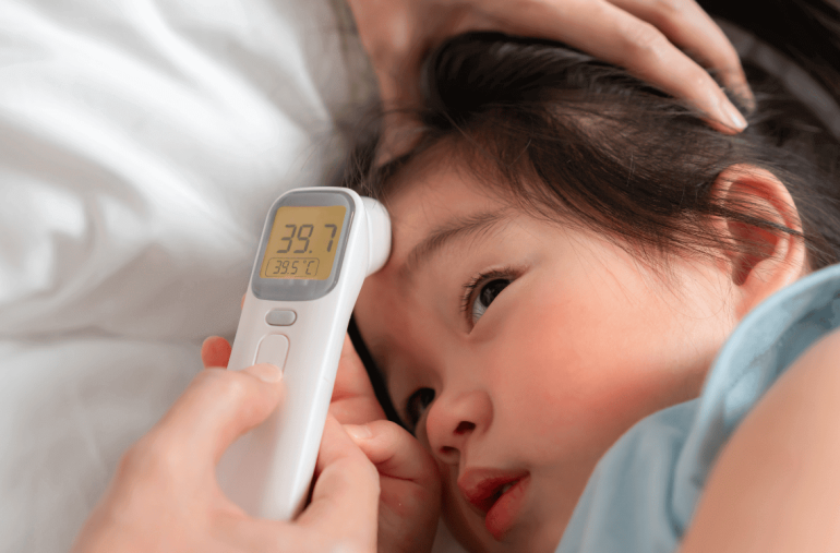 A caring parent checks the temperature of a young child using a digital thermometer at home, highlighting concern and the importance of monitoring health during illness.