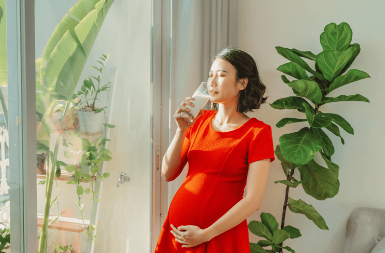 pregnant woman drinking milk when standing behind the window