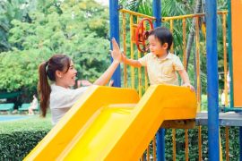 child playing with mother in the playground going down the yellow slide