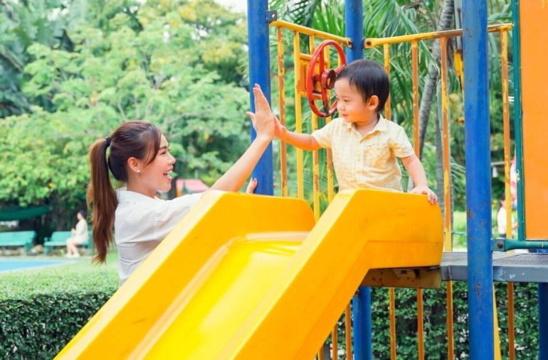 child playing with mother in the playground going down the yellow slide