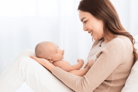 mother supports and tenderly cuddles the newborn baby gently while infant lying on lap