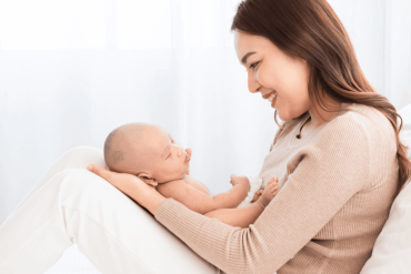 mother supports and tenderly cuddles the newborn baby gently while infant lying on lap