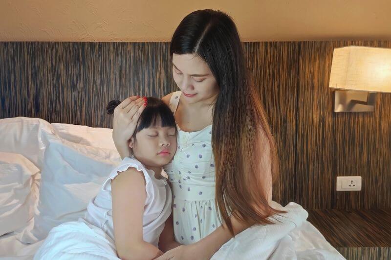 Mother is hugging her daughter to comfort her when she is sick on white bed.