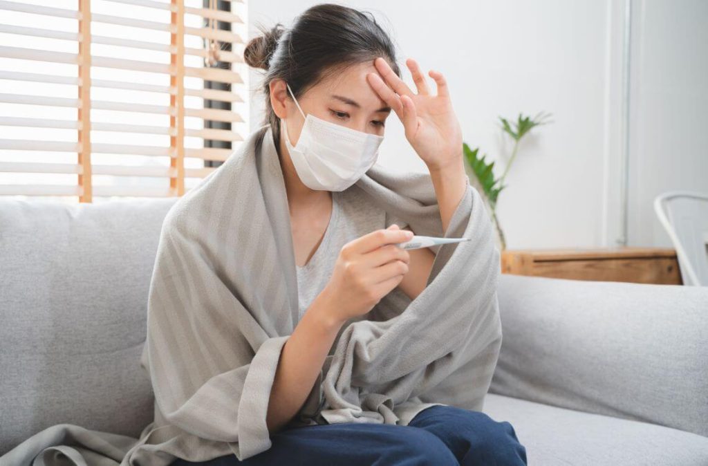 Sick day at home in winter season. Young asian woman have a fever checking thermometer and measure body temperature.