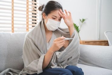 Sick day at home in winter season. Young asian woman have a fever checking thermometer and measure body temperature.