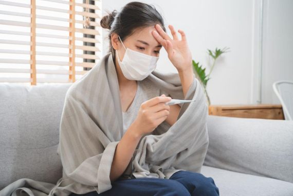 Sick day at home in winter season. Young asian woman have a fever checking thermometer and measure body temperature.