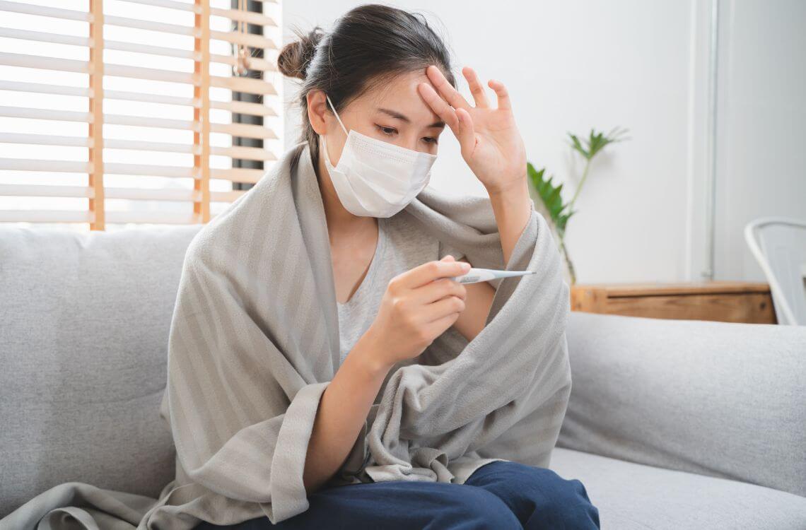 Sick day at home in winter season. Young asian woman have a fever checking thermometer and measure body temperature.